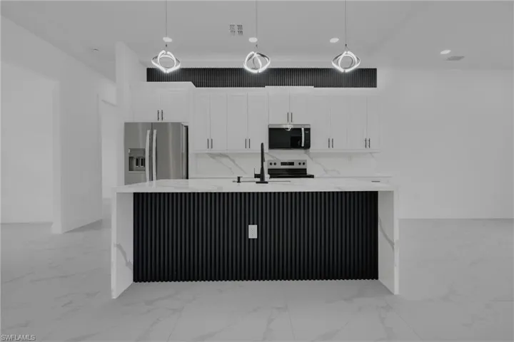 Modern kitchen featuring a waterfall island with a slatted black base, white cabinetry, integrated stainless steel appliances, and sleek pendant lighting