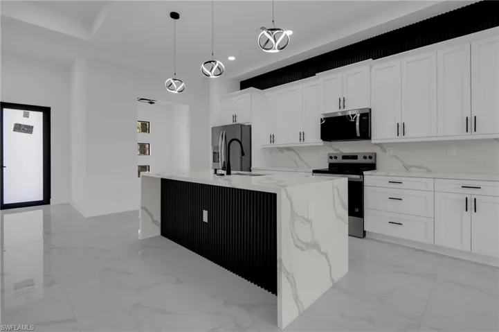 Modern kitchen featuring white shaker cabinetry with matte black hardware, integrated stainless steel appliances, a waterfall island with a fluted black base, and a tiled backsplash