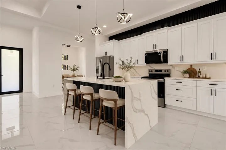 Gourmet kitchen with an expansive waterfall island, white shaker cabinetry, stainless steel appliances, and a tray ceiling