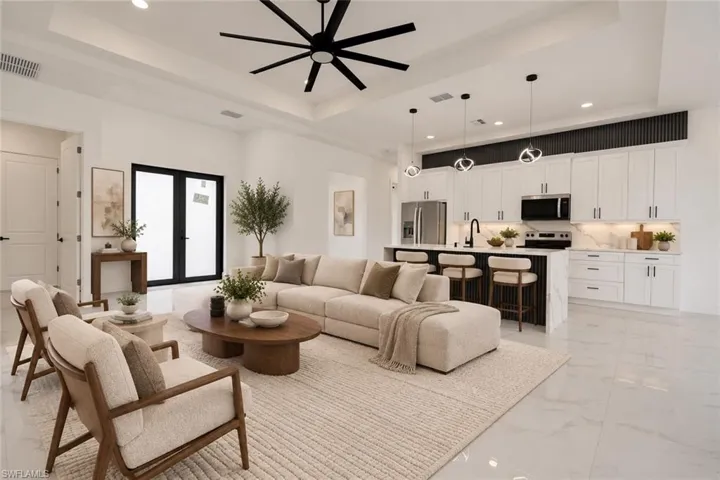 Open-concept living area featuring a kitchen island, stainless steel appliances, white cabinetry, and large format floor tiles