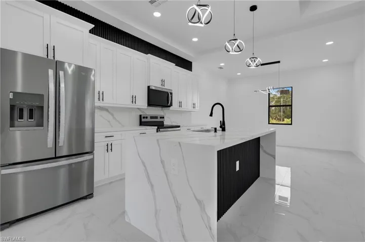 Modern kitchen featuring white shaker cabinetry, stainless steel appliances, a large center island with a waterfall countertop, and contemporary pendant lighting