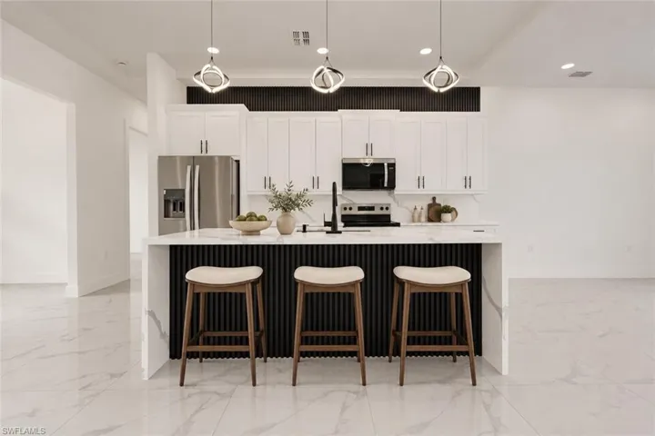 Kitchen featuring a waterfall island with fluted paneling, white shaker cabinetry, stainless steel appliances, and pendant lighting