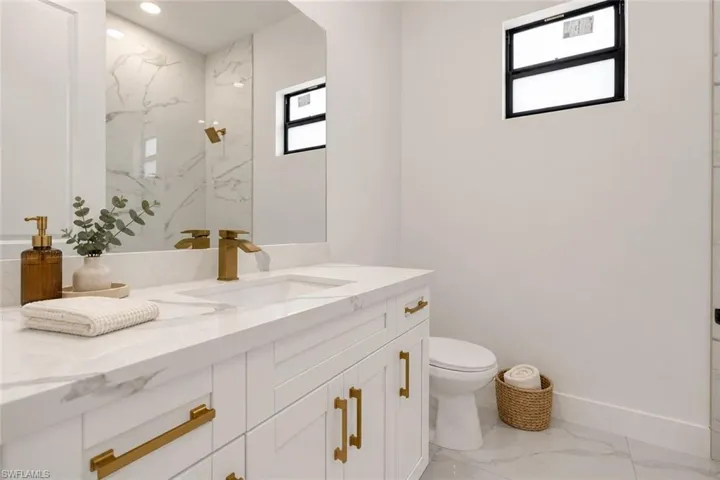 White vanity with gold-tone hardware, undermount sink, and stone-look countertop