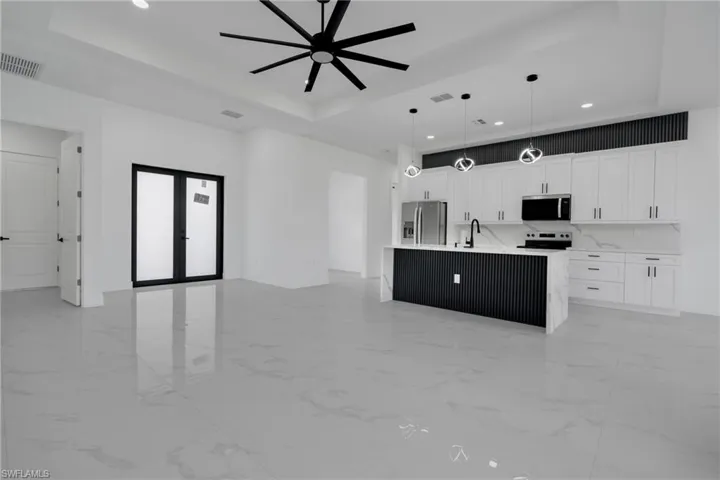 Open-concept living space featuring a contemporary kitchen with white cabinetry, stainless steel appliances, and a central island with a waterfall countertop