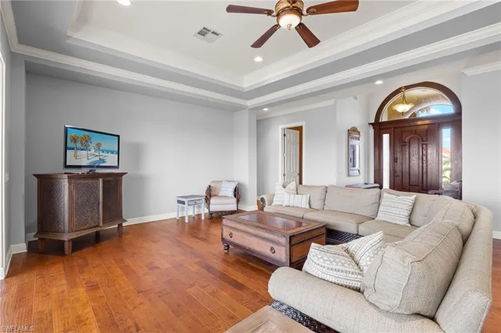 Living room with hardwood / wood-style floors, crown molding, a tray ceiling, and ceiling fan