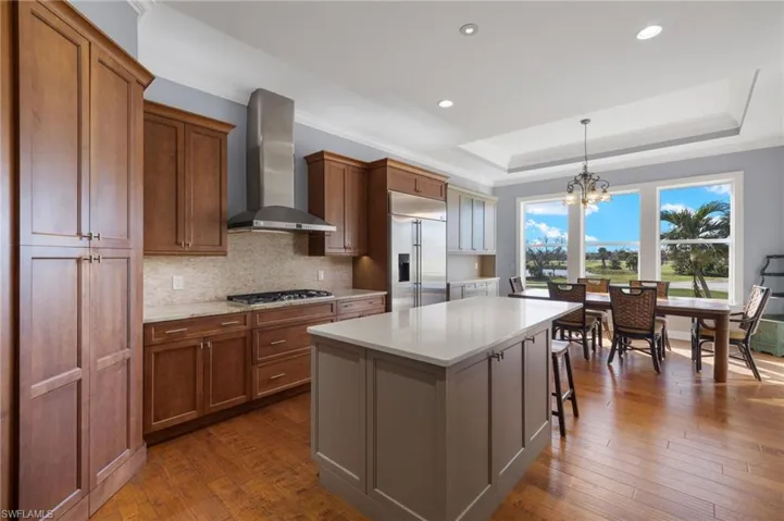 Kitchen with appliances with stainless steel finishes, a kitchen island, hanging light fixtures, wall chimney exhaust hood, and dark hardwood / wood-style floors