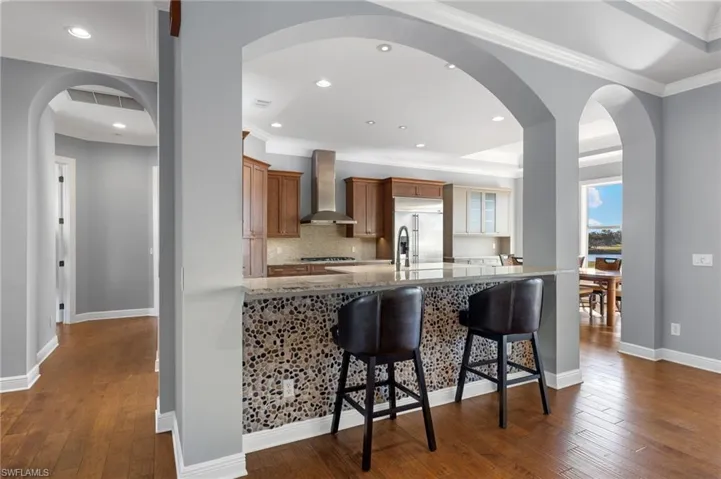 Kitchen featuring wall chimney range hood, ornamental molding, built in refrigerator, decorative backsplash, and dark hardwood / wood-style floors