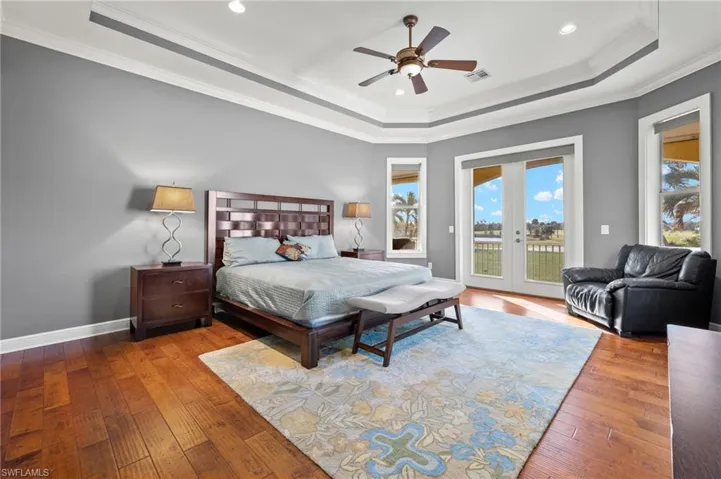 Bedroom with wood-type flooring, a tray ceiling, access to exterior, ceiling fan, and crown molding