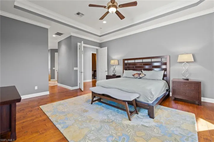 Bedroom featuring dark hardwood / wood-style flooring, crown molding, a raised ceiling, and ceiling fan