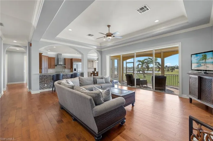 Living room featuring ceiling fan, crown molding, wood-type flooring, and a raised ceiling