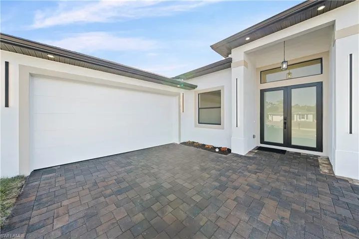 View of exterior entry with decorative driveway, french doors, a garage, and stucco siding
