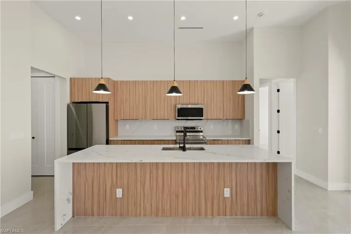Kitchen with light stone countertops, modern cabinets, pendant lighting, a high ceiling, and a large island with sink