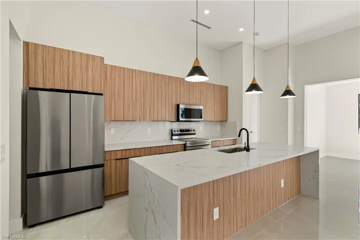 Kitchen featuring light stone counters, stainless steel appliances, decorative light fixtures, modern cabinets, and backsplash