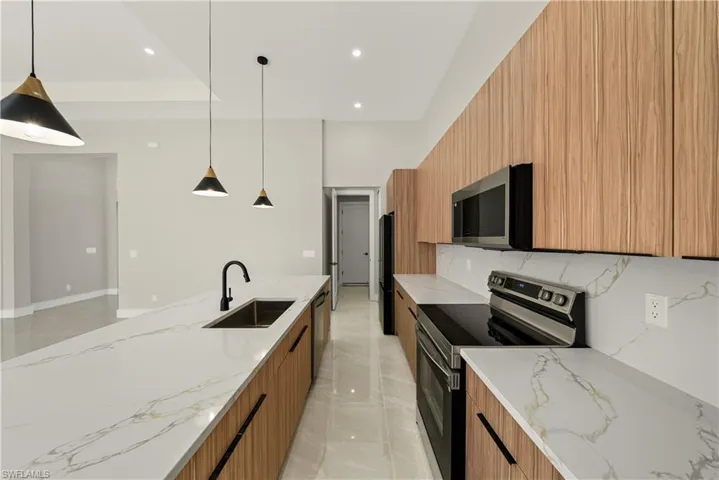 Kitchen with modern cabinets, light stone counters, stainless steel appliances, and pendant lighting