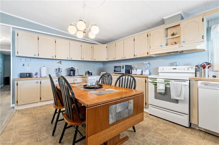Kitchen featuring white appliances, light countertops, vaulted ceiling, ornamental molding, and open shelves