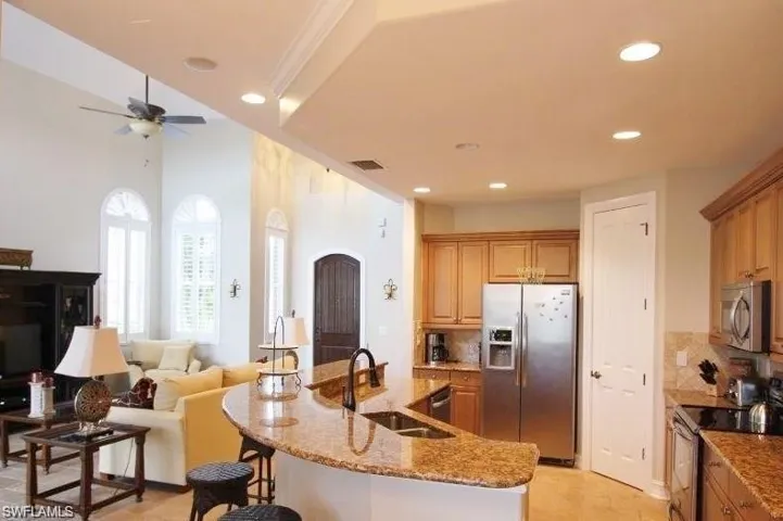 Kitchen with stainless steel appliances, open floor plan, a center island with sink, light stone counters, and decorative backsplash