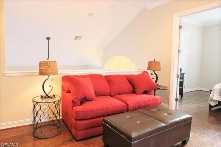 Living area with dark wood-type flooring, crown molding, and lofted ceiling