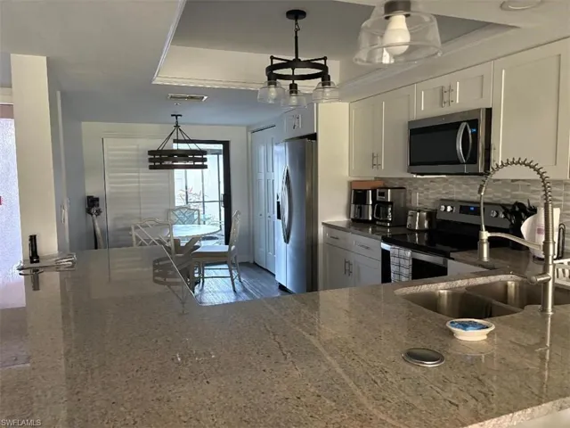 Kitchen featuring stainless steel appliances, dark stone counters, white cabinets, decorative light fixtures, and a peninsula