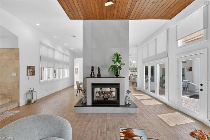 Bright living area featuring a fireplace with a stone surround, wood flooring, and a wood-paneled ceiling accent