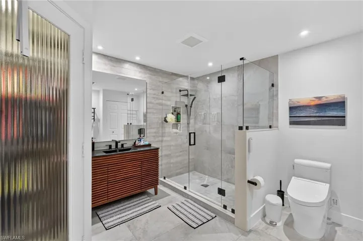 Bathroom featuring a modern vanity with a dark countertop and dual sinks, a spacious glass-enclosed shower with tile walls, and recessed lighting