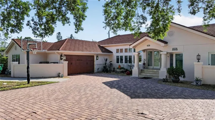 The property features a paver driveway, an attached garage with a wooden door, and a covered entry with double doors and decorative columns