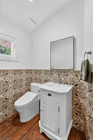 Bathroom featuring decorative tile work, a white vanity with a built-in sink, and wood-look flooring