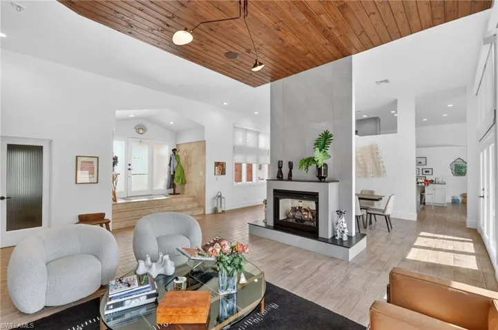 This spacious living area features a high vaulted wood-paneled ceiling, light-toned flooring, and a modern fireplace with a light-colored surround