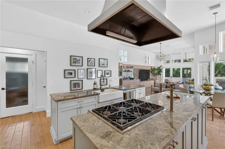 The kitchen features a large island with a gas cooktop, stone countertops, and a white farmhouse sink