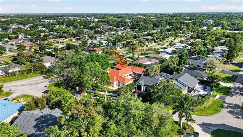 The property features a red tile roof and is surrounded by mature trees, situated within a neighborhood characterized by lush greenery and a variety of residential architecture