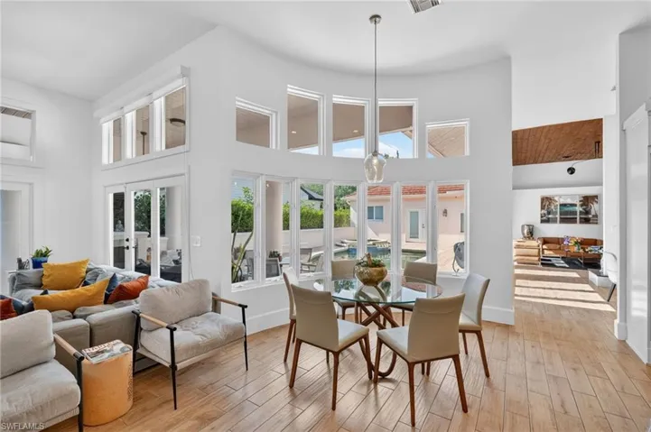Bright, open concept living area featuring light-colored flooring, tall ceilings, and expansive windows providing abundant natural light and views of the outdoor pool area