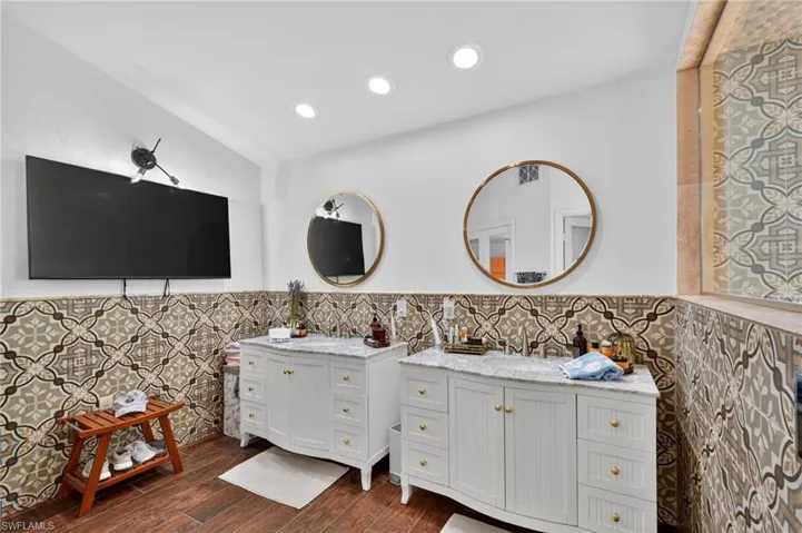 The bathroom features two white vanities with marble countertops, round mirrors, and patterned wall tiles