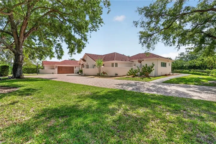 The property features a large paved driveway, a well-maintained lawn, and mature trees providing shade