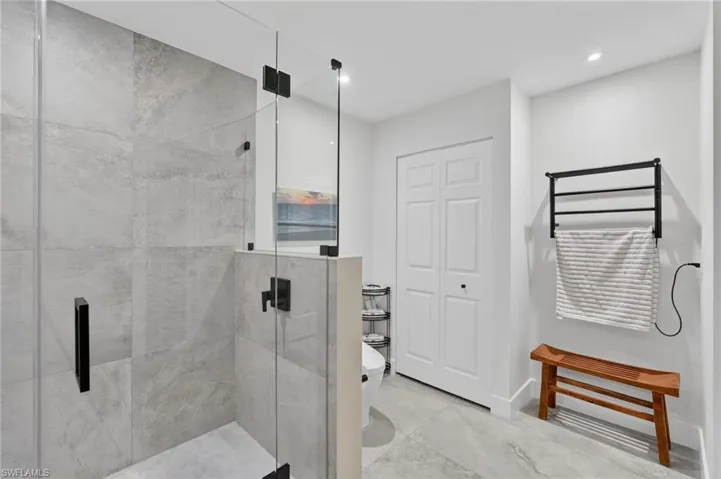 Bathroom featuring a glass-enclosed shower with large format grey tile, a white bi-fold door, and a wall-mounted towel warmer