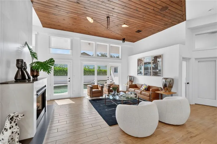 This sophisticated living area features a distinctive wood-paneled ceiling, large windows, and glass doors that provide views of an outdoor area with water