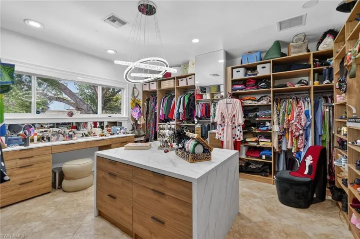 The property features an expansive closet with custom wooden shelving and hanging storage, a central island with a white marble-look countertop and wooden drawers, and a built-in vanity area with a long window providing natural light
