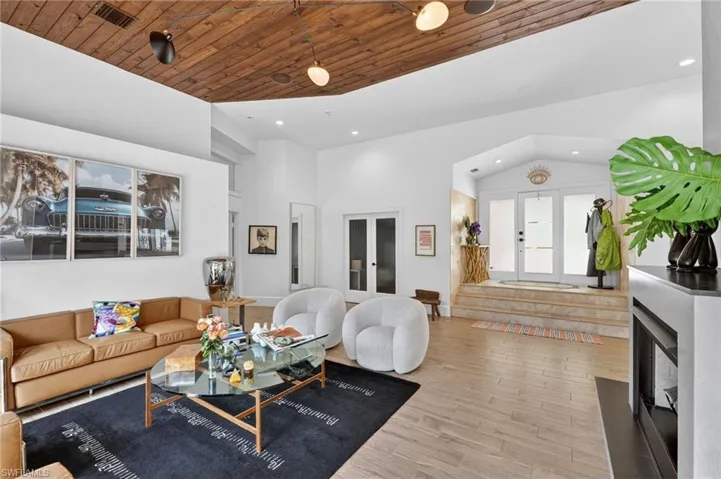 The spacious living area features a wood-paneled ceiling, light-toned flooring, and a fireplace with a dark mantel