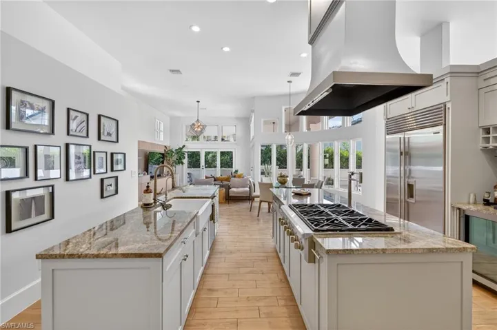 The kitchen features two spacious islands with granite countertops and white cabinetry, complemented by stainless steel appliances including a large refrigerator and range