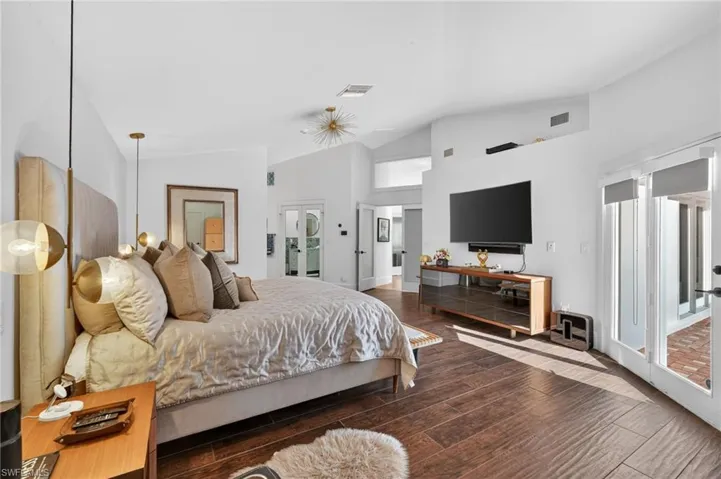 Spacious bedroom featuring dark wood-style flooring, white walls, vaulted ceilings, and direct outdoor access through glass panel doors