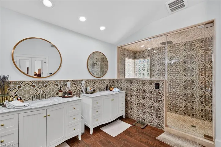 The bathroom features dual vanities with white cabinetry and marble countertops, round mirrors, and patterned tile work