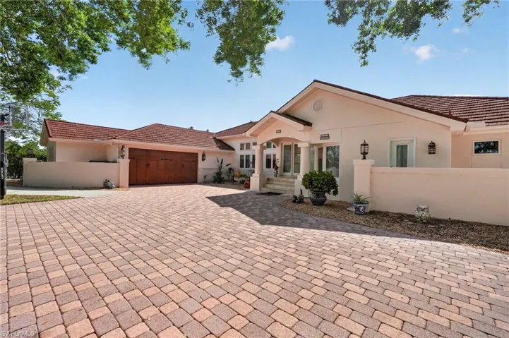 The property features a paver driveway, a two-car garage with a wooden door, and a covered entryway with columns