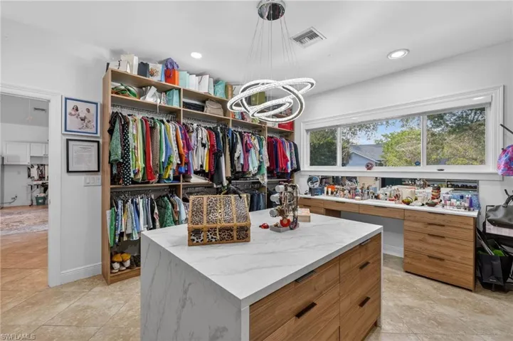 Spacious dressing area featuring custom built-in shelving, a large central island with drawers and a countertop, and a window providing natural light