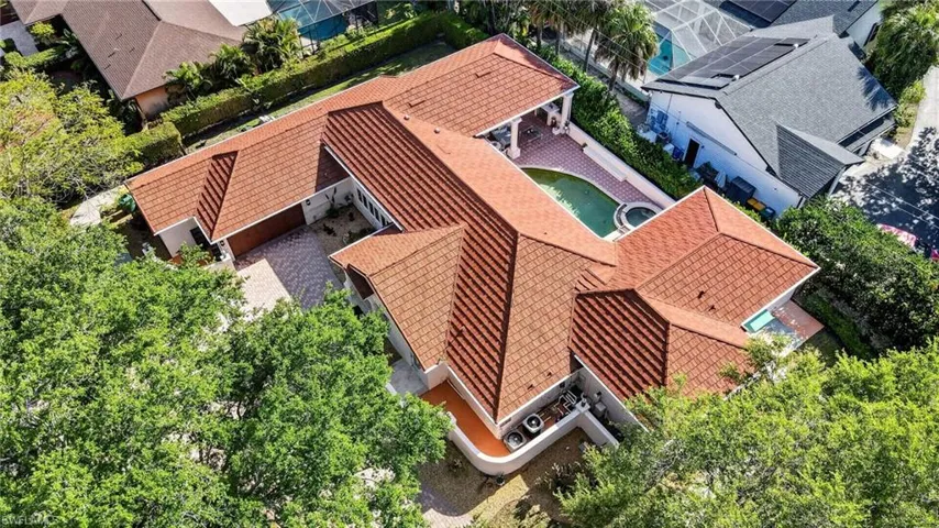 Aerial view of the property showcasing the distinctive red tile roof, expansive patio area, and a swimming pool with an integrated spa
