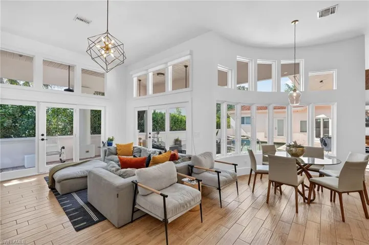 The living area features high ceilings, hardwood flooring, and abundant natural light from numerous windows and glass doors
