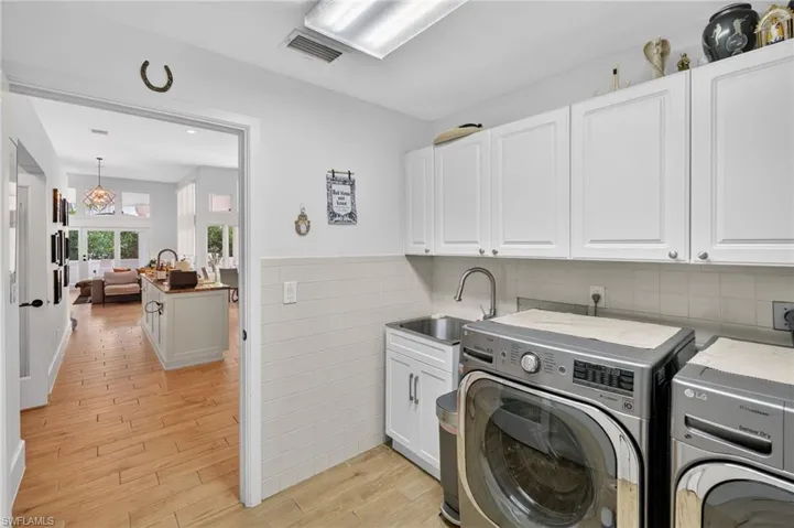 This laundry area features white cabinetry, a utility sink, and light-colored tile flooring