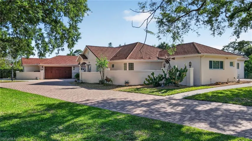 The property features a red tile roof, an attached garage with a wooden door, and a paved driveway