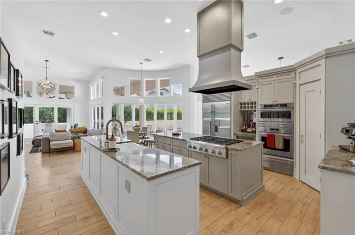 The kitchen features two islands with granite countertops, light wood flooring, stainless steel appliances, and extensive cabinetry