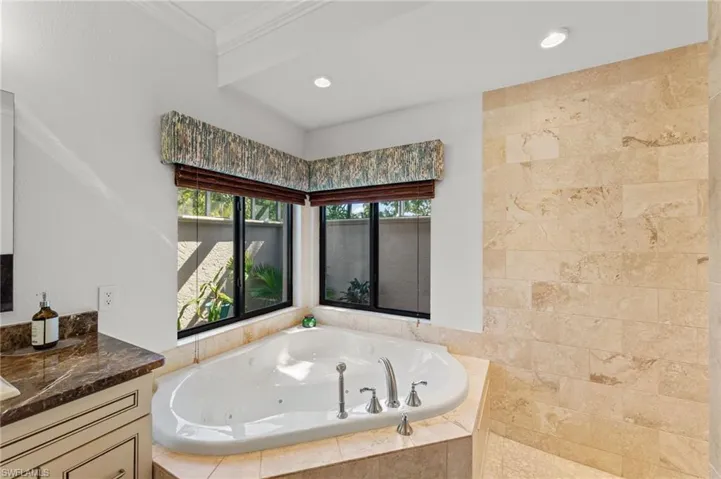 Bathroom with a tub with jets, vanity, crown molding, and recessed lighting