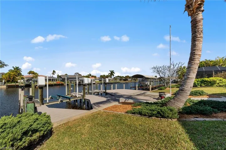Dock with boat lift, a water view, a yard, and a residential view