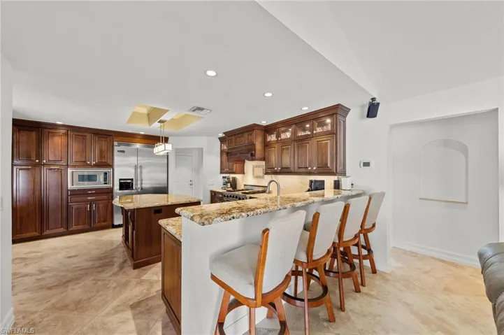 Kitchen with a breakfast bar, a peninsula, built in appliances, light stone countertops, and a kitchen island