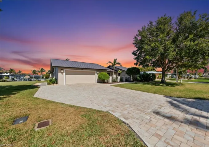 View of front facade with a front yard, decorative driveway, a metal roof, and an attached garage